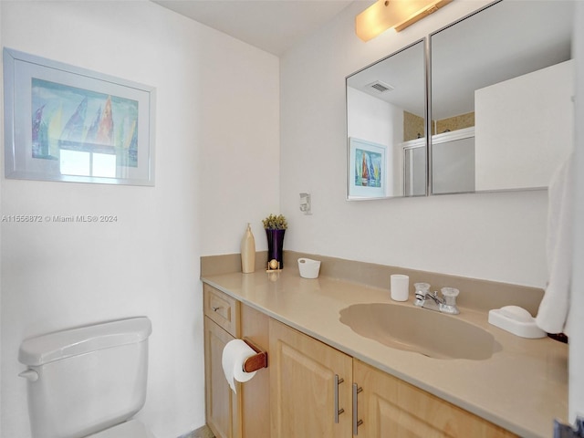 bathroom featuring a shower with shower door, vanity, and toilet