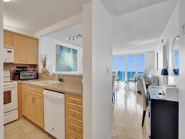 kitchen featuring light brown cabinets, sink, white appliances, a textured ceiling, and a water view