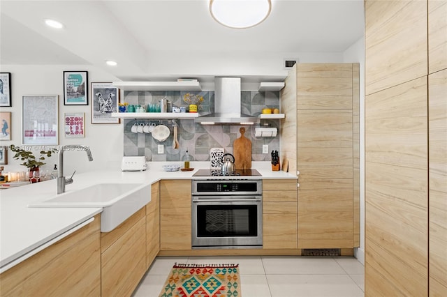 kitchen with stainless steel oven, black electric cooktop, light tile floors, wall chimney range hood, and sink