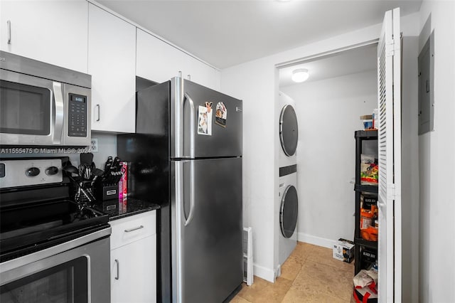 kitchen featuring white cabinetry, stacked washer / dryer, appliances with stainless steel finishes, light tile floors, and dark stone countertops