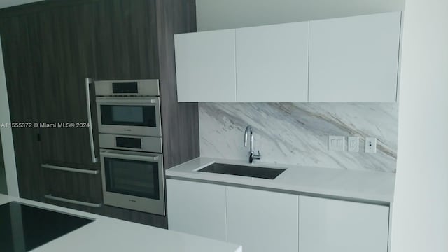 kitchen featuring double oven, sink, white cabinetry, and tasteful backsplash