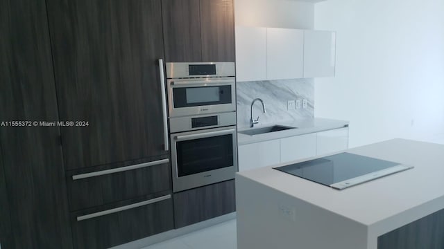 kitchen with double oven, black electric stovetop, backsplash, white cabinets, and sink