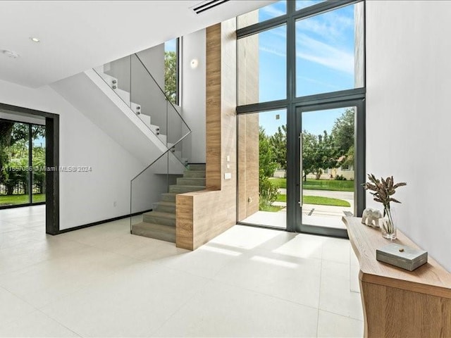 doorway to outside with light tile patterned floors, a towering ceiling, and expansive windows