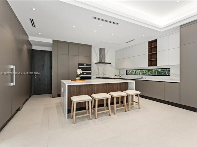 kitchen with double oven, tasteful backsplash, light tile patterned floors, a large island, and wall chimney range hood