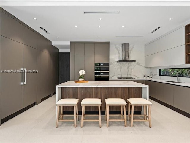 kitchen featuring a center island, sink, double oven, wall chimney exhaust hood, and light tile patterned floors