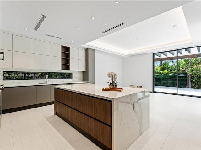 kitchen with a center island, light tile patterned flooring, a raised ceiling, and white cabinets