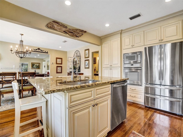 kitchen featuring a chandelier, dark hardwood / wood-style floors, stainless steel appliances, a kitchen island with sink, and cream cabinets