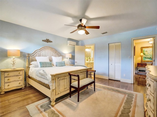 bedroom featuring ceiling fan, connected bathroom, light hardwood / wood-style flooring, and a wall unit AC