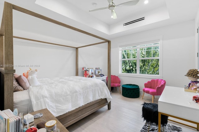 bedroom featuring a tray ceiling, ceiling fan, and light wood-type flooring