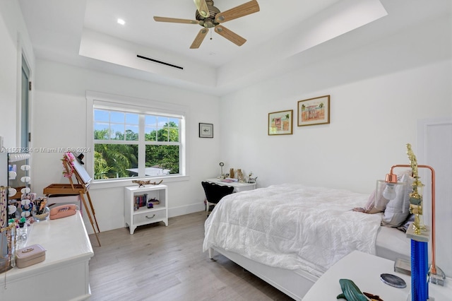 bedroom with a tray ceiling, ceiling fan, and light wood-type flooring