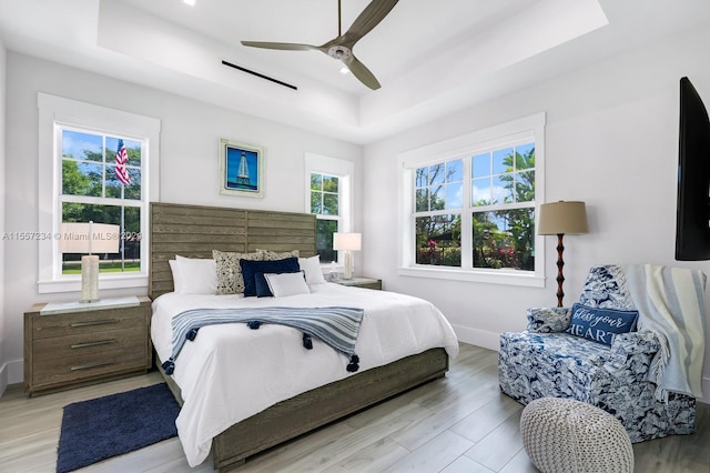 bedroom featuring ceiling fan, a raised ceiling, and light hardwood / wood-style flooring