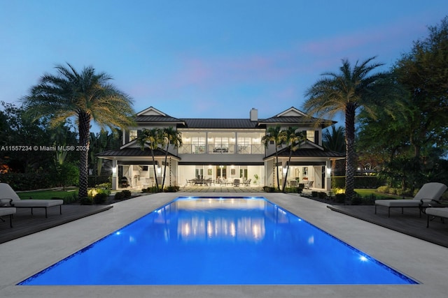 pool at dusk with outdoor lounge area and a patio