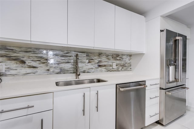 kitchen with appliances with stainless steel finishes, sink, light tile floors, white cabinets, and tasteful backsplash