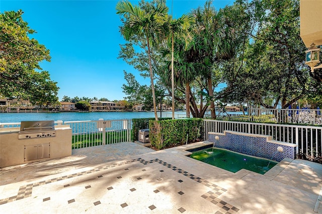 view of pool featuring an outdoor kitchen, grilling area, a water view, fence, and a patio area