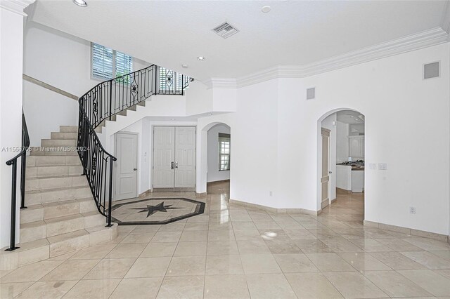 entrance foyer featuring ornamental molding, light tile patterned floors, and a high ceiling