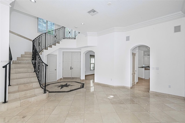 foyer featuring visible vents, arched walkways, baseboards, a towering ceiling, and stairs