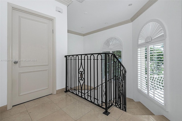 hall with tile patterned flooring, ornamental molding, and an upstairs landing