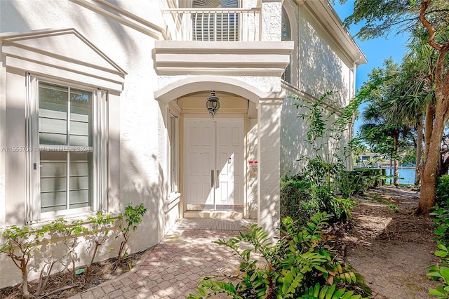 view of exterior entry with a balcony and stucco siding