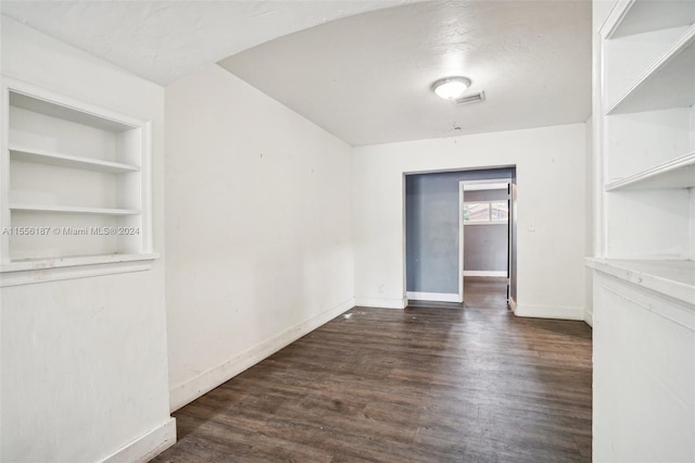 spare room with dark hardwood / wood-style flooring, built in features, and a textured ceiling