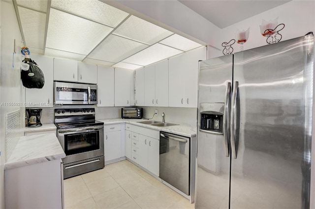 kitchen featuring appliances with stainless steel finishes, sink, light tile patterned floors, and white cabinets