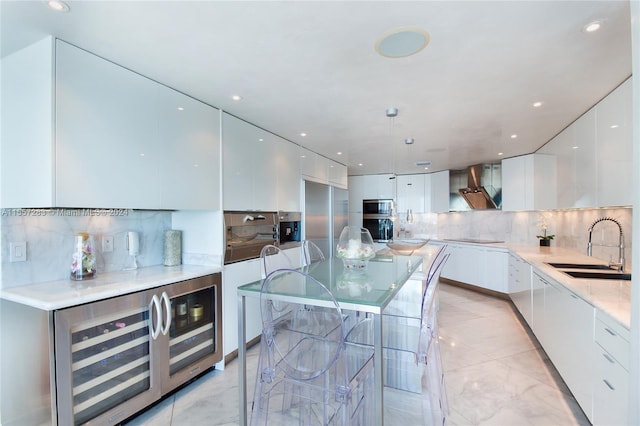 kitchen with sink, light tile flooring, wall chimney range hood, tasteful backsplash, and white cabinetry