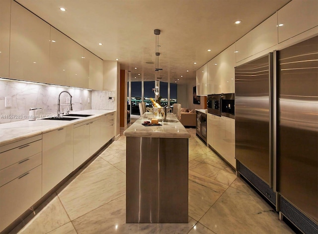 kitchen with high end refrigerator, a center island with sink, backsplash, and light tile flooring