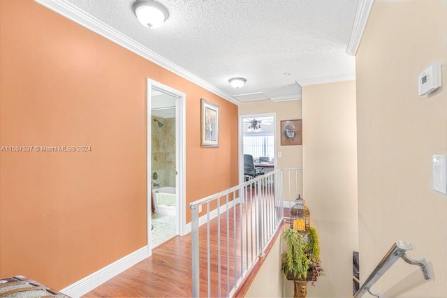 corridor with a textured ceiling, crown molding, and light hardwood / wood-style floors