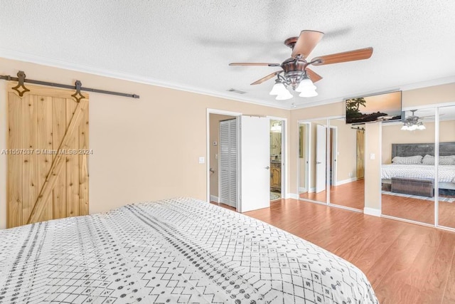 bedroom featuring a barn door, ornamental molding, light hardwood / wood-style floors, and ceiling fan