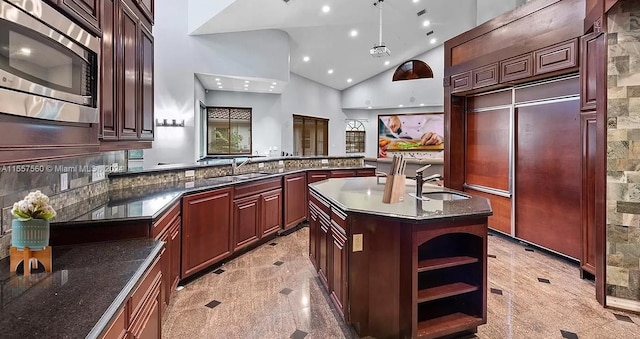 kitchen featuring hanging light fixtures, stainless steel microwave, high vaulted ceiling, sink, and a center island with sink