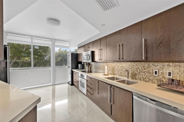 kitchen featuring appliances with stainless steel finishes, sink, light tile floors, tasteful backsplash, and dark brown cabinetry