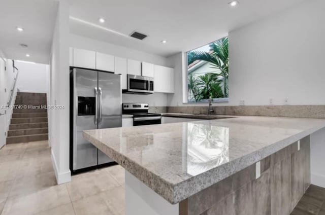 kitchen with white cabinets, appliances with stainless steel finishes, light stone countertops, sink, and kitchen peninsula