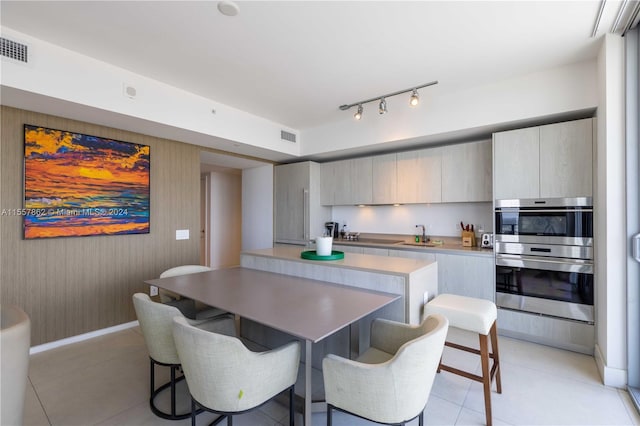 kitchen with stainless steel double oven, light tile flooring, rail lighting, and a breakfast bar area