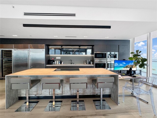 kitchen with a wall of windows, black appliances, a kitchen island, wood counters, and a breakfast bar area