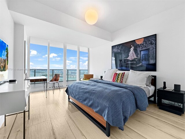 bedroom with a water view, expansive windows, and light hardwood / wood-style floors