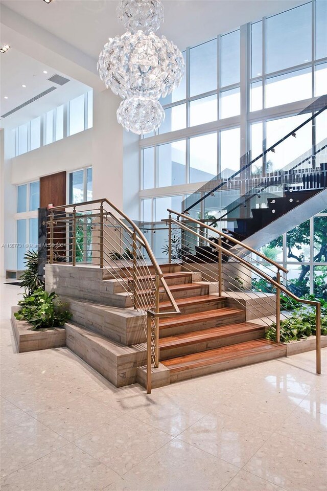 staircase featuring a healthy amount of sunlight, a high ceiling, and an inviting chandelier