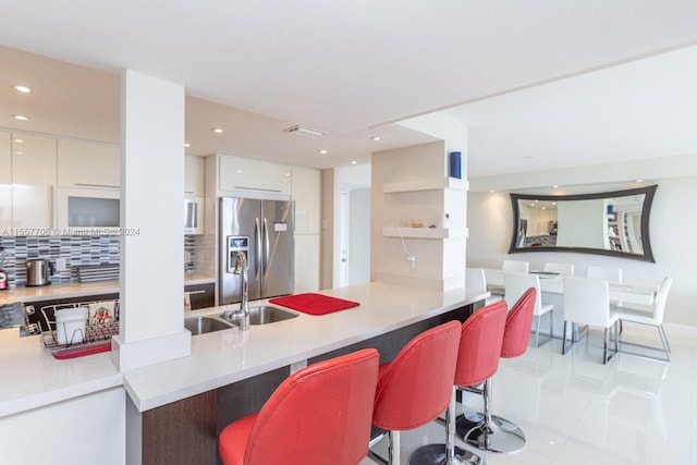 kitchen with light tile flooring, a kitchen bar, white cabinetry, backsplash, and stainless steel refrigerator with ice dispenser