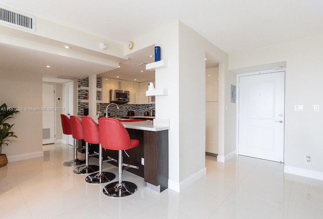 kitchen with an island with sink, light brown cabinets, light tile floors, a breakfast bar, and backsplash