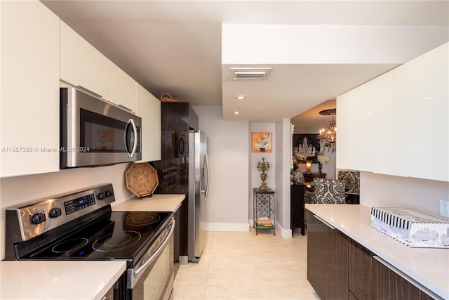 kitchen featuring an inviting chandelier, stainless steel appliances, light tile flooring, and white cabinetry