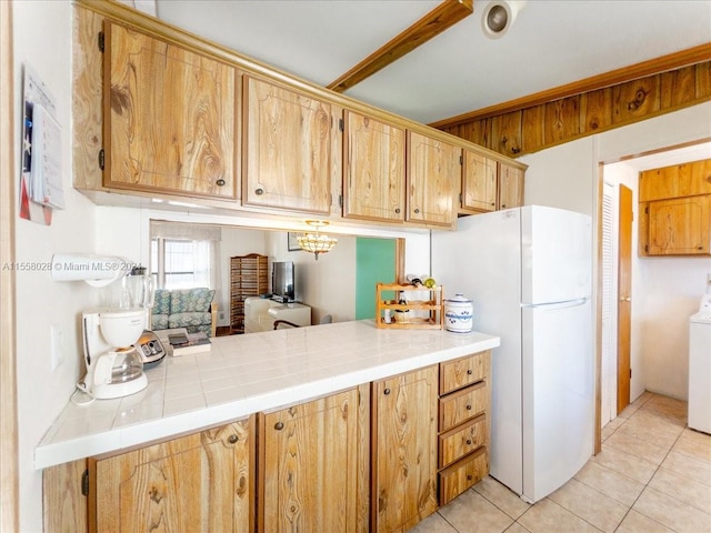 kitchen featuring light tile floors, white refrigerator, tile countertops, washer / clothes dryer, and a notable chandelier