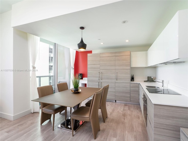 kitchen featuring stainless steel oven, black electric stovetop, light brown cabinetry, light hardwood / wood-style floors, and pendant lighting