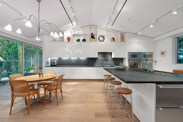 kitchen featuring pendant lighting, decorative backsplash, rail lighting, and an island with sink