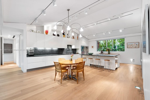 dining room featuring lofted ceiling, sink, light hardwood / wood-style flooring, and track lighting