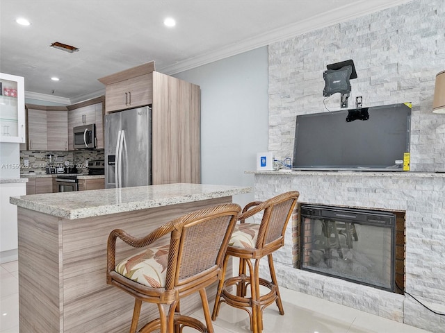 kitchen with ornamental molding, a breakfast bar, appliances with stainless steel finishes, and light stone counters