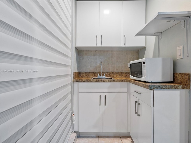 kitchen featuring sink, light tile floors, dark stone counters, white cabinets, and tasteful backsplash