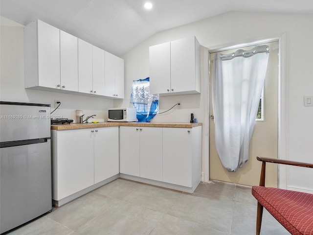 kitchen featuring light tile floors, white cabinets, vaulted ceiling, and stainless steel refrigerator