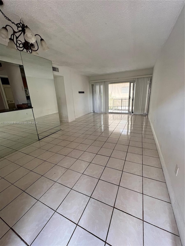 empty room with an inviting chandelier, a textured ceiling, and light tile floors