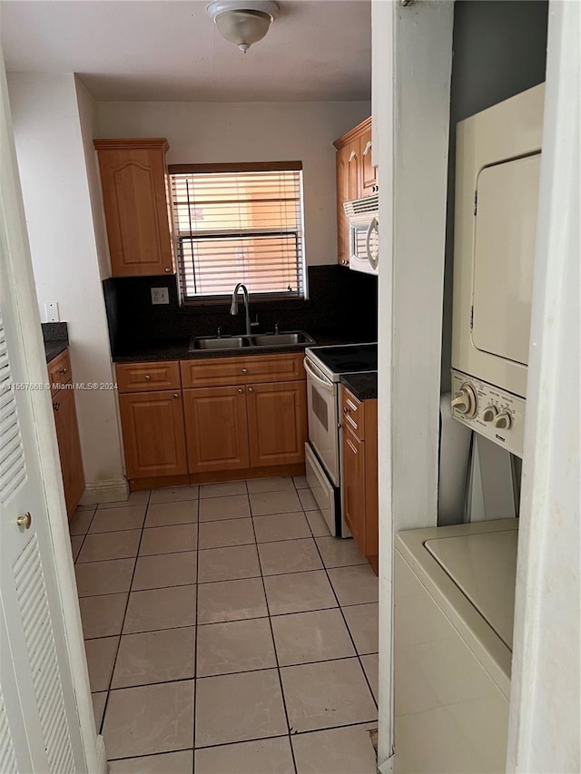 kitchen featuring stacked washer and dryer, tasteful backsplash, white appliances, sink, and light tile flooring