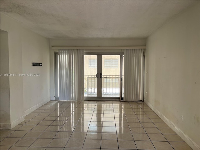 empty room featuring a textured ceiling, french doors, and light tile flooring