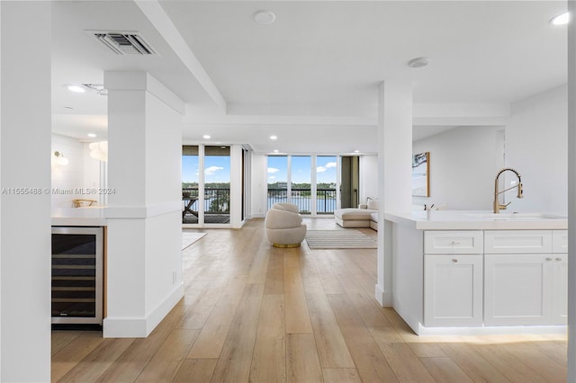 interior space with white cabinets, wine cooler, light wood-type flooring, sink, and a wall of windows