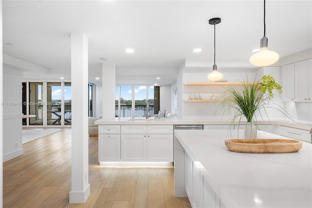 kitchen with white cabinets, light stone countertops, light wood-type flooring, decorative light fixtures, and sink